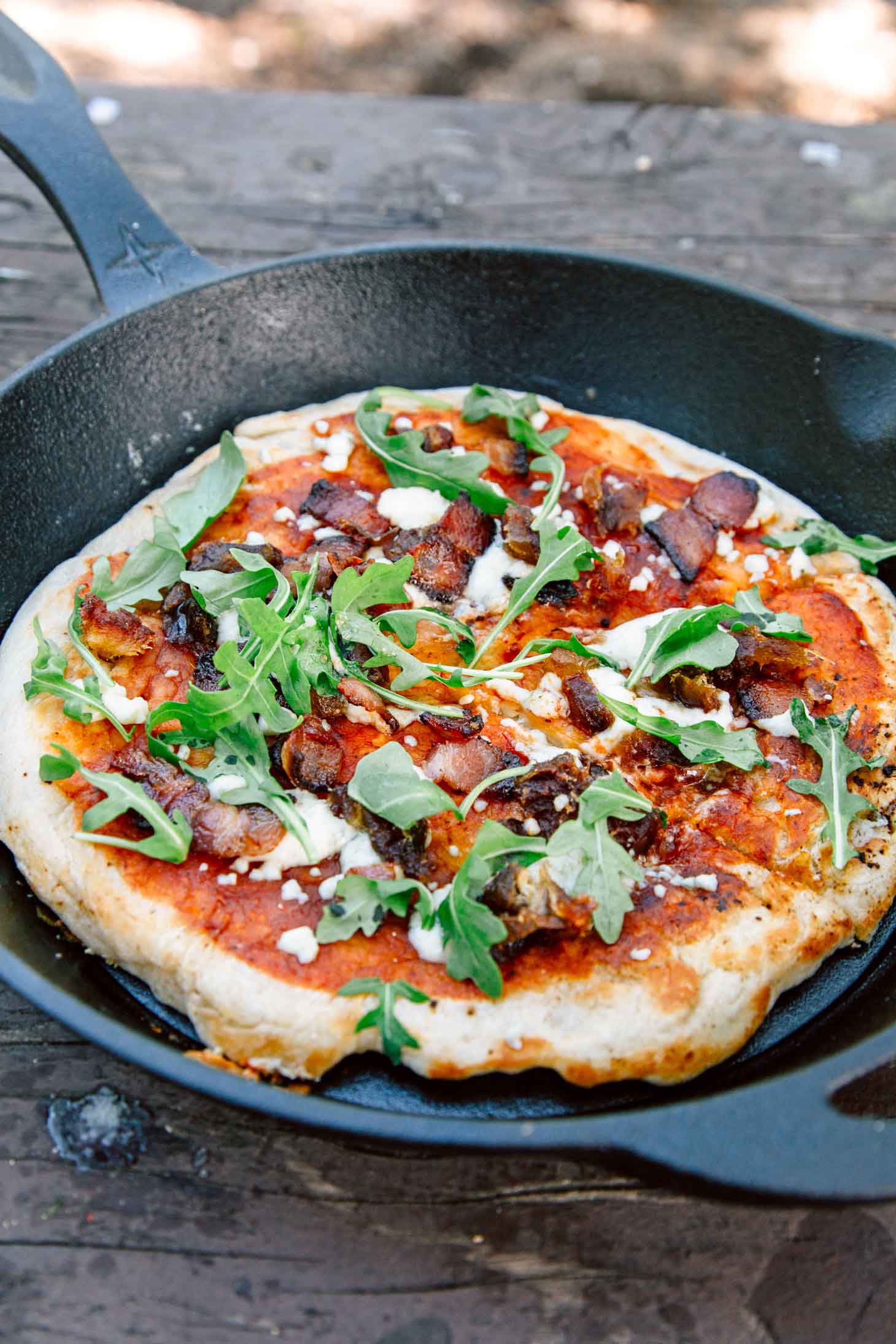 30 Best camping meals ever! A cast iron skillet holding a pizza with bacon, dates and arugula 