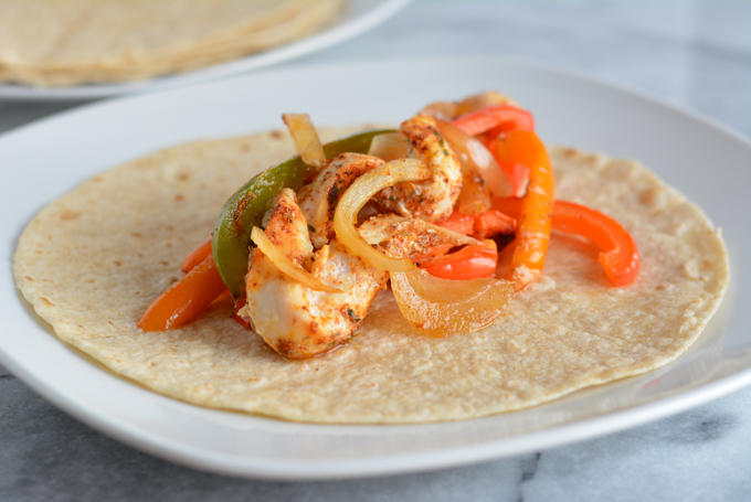 Sheet pan dinners are getting more and more popular because of the ease of effort and convenience they're affording people with super busy lives! Chicken with peppers and onions on a tortilla on a plate.